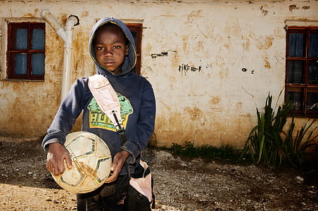 boy in blue hoodie holding soccer ball near building thumbnail