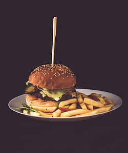 brown hamburger with lettuce and tomato with french fries on white ceramic plate thumbnail