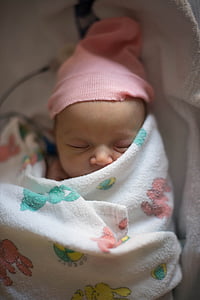 sleeping baby wearing orange knit cap with white and multicolored blanket thumbnail