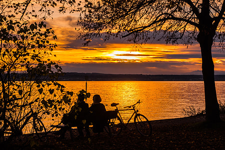silhouette photo of people sitting on bench facing body of water thumbnail