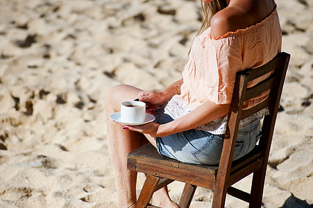 woman sitting on wooden chair holding white mug and saucer thumbnail