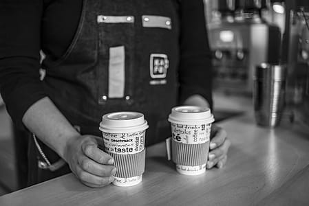 Grayscale Photo of Person Holding Disposable Cups thumbnail