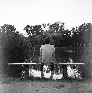 grayscale photography of man in shirt sit on bench in front of lake thumbnail
