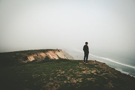 man standing beside cliff near body of water during daytime thumbnail