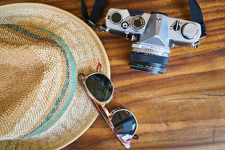 black and gray DSLR camera beside a sunglasses and hat on table thumbnail