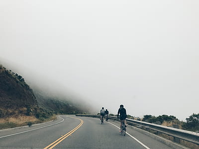 three people biking on road near cliff with fog thumbnail