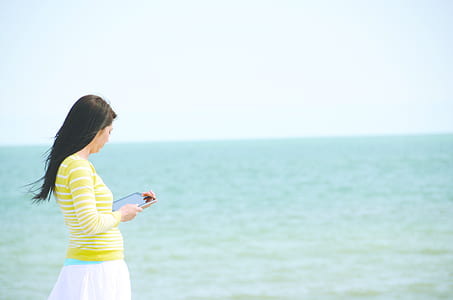 Woman In Yellow Long Sleeved Shirt And White Skirt Walking On Seashore thumbnail