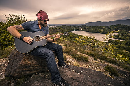 man playing black acoustic guitar sitting on rock thumbnail