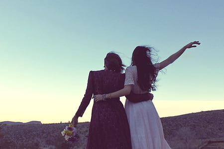 two women standing under the cliff during daytime thumbnail
