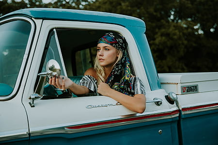 woman in white and grey shirt sitting inside pickup truck while looking mirror during daytime thumbnail