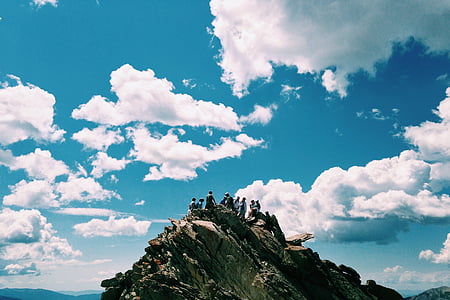 people standing on mountain cliff under cloudy sky thumbnail