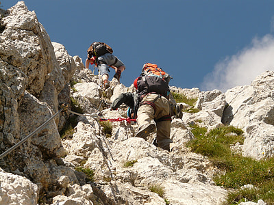 person carrying orange hiking backpack climbing white rocks thumbnail