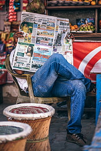 tilt shift lens photography of man wearing blue jeans while holding newspaper thumbnail