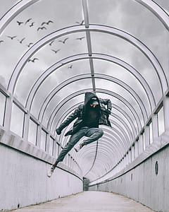 man wearing black zip-up hoodie jump mid-air on gray concrete hallway during daytime thumbnail