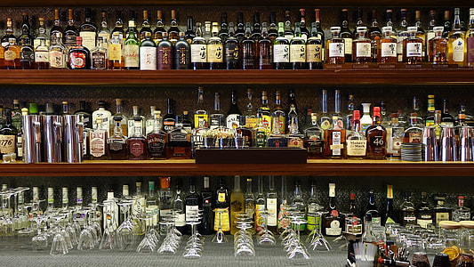 assorted alcoholic beverage bottles and wine glasses on brown wooden shelf thumbnail