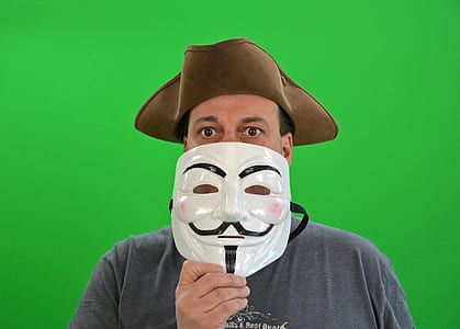 man wearing brown hiking hat holding Guy Fawkes mask thumbnail
