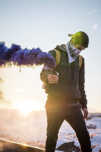 person in gray zip-up hoodie holding smoke bomb walking during sunset thumbnail