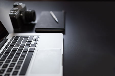 MacBook Pro beside camera, notebook and pen thumbnail