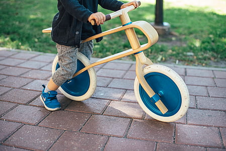 boy riding brown wooden balance bike on bricked pavement during daytime thumbnail