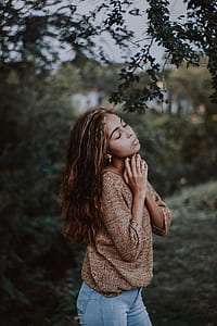 woman in brown long-sleeved top and blue jeans under green leafed tree thumbnail