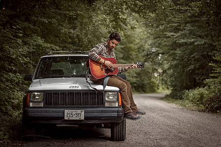 man playing guitar sitting on engine hood during daytime thumbnail