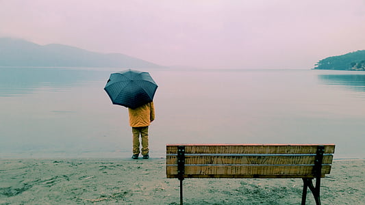 person holding black umbrella standing in front of ocean thumbnail