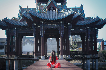 woman in red dress sitting on brown dock near black temple gate at daytime thumbnail