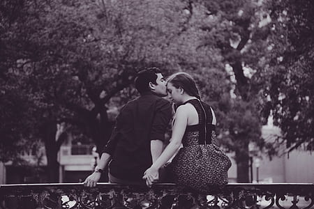grayscale photography of couple sitting on fence while men kissing woman's forehead thumbnail