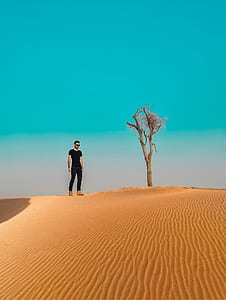 man standing on desert near tree during daytime thumbnail