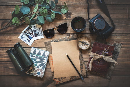 sunglasses, camera, binocular with pen and cards on brown wooden surface thumbnail