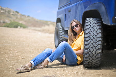 Woman in Yellow Polo Shirt Sitting on Ground Leaning on Blue Vehicle at Daytime thumbnail