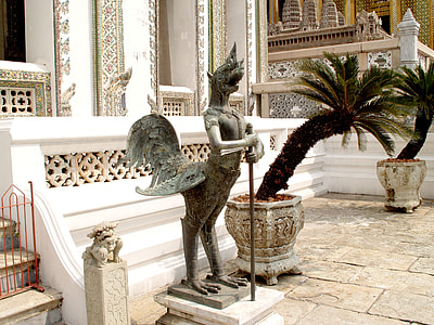 statue holding rod beside plants during daytime thumbnail