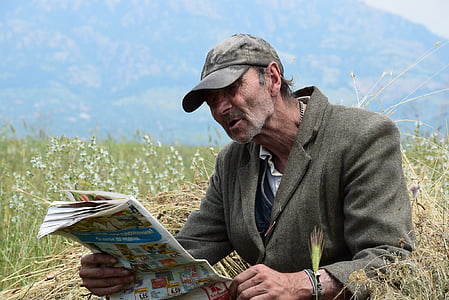 man in gray coat reading newspaper during daytime thumbnail