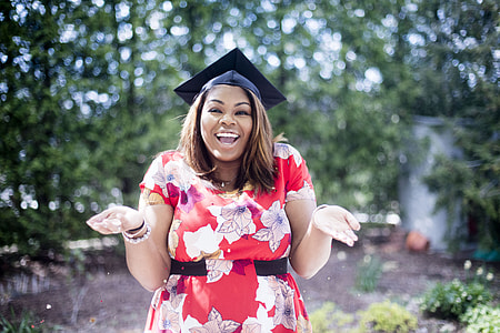woman in floral dress with two open palms wearing academic cap outdoors thumbnail