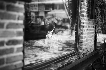 grayscale photo of man sitting inside the building near glass window thumbnail