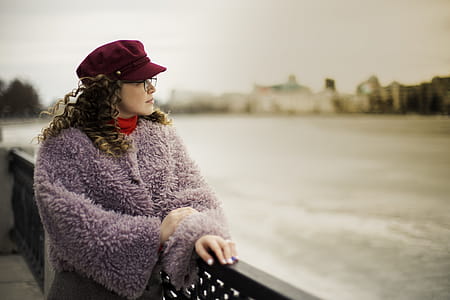 Woman Wearing Purple Fleece Coat Standing Beside Black Metal Fence Near Body of Water thumbnail