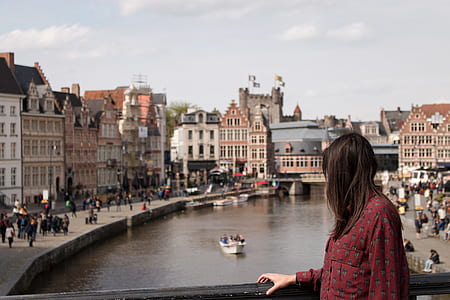 woman holding black steel fence surrounded by concrete buildings and river outdoors thumbnail