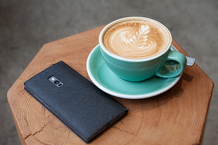 cup of latte beside black Android smartphone on brown wooden table thumbnail
