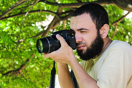Man in Beige Shirt Taking Photo Using Black Dslr Camera Beside Tree thumbnail