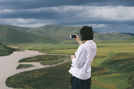 woman taking picture of green lands using smartphone at daytime thumbnail