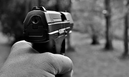 grayscale photography of a person holding black semi-automatic pistol thumbnail
