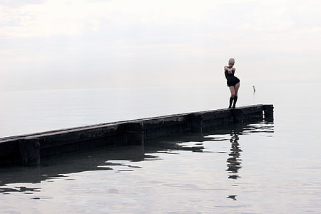 woman in black sleeveless mini dress standing on sea dock during daytime thumbnail