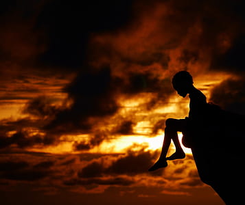 silhouette photography of child sitting on rock during golden hour thumbnail