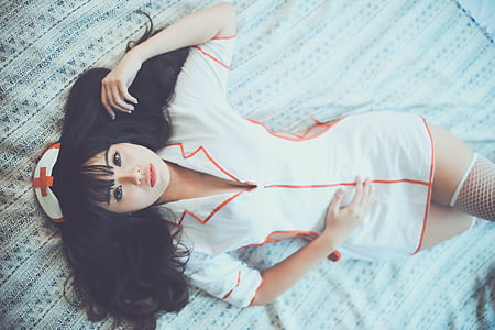 woman with white-and-orange nurse uniform laid on white lace textile thumbnail