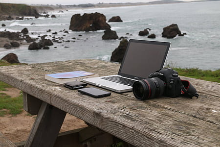 MacBook Pro with turned-off screen near DSLR camera on table thumbnail