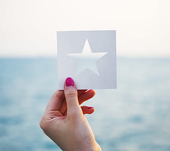 A female hand holding a star shaped paper cut out template with ocean in the background thumbnail