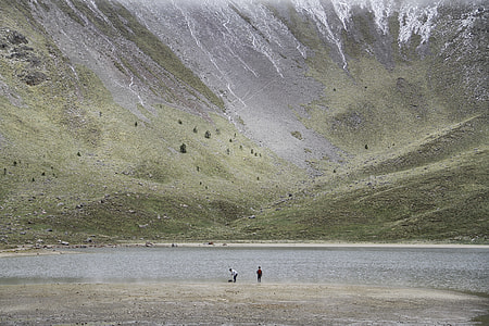 two person standing near body of water near mounatin thumbnail