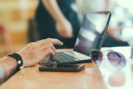 black laptop beside black smartphone and purple sunglasses with gold-colored frames on brown wooden desk thumbnail