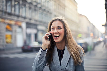 A young blonde woman wearing a checkered coat calling on her mobile phone in the street thumbnail