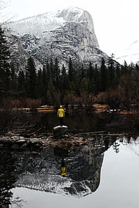 person in yellow hoodie standing on rock in front of body of water thumbnail